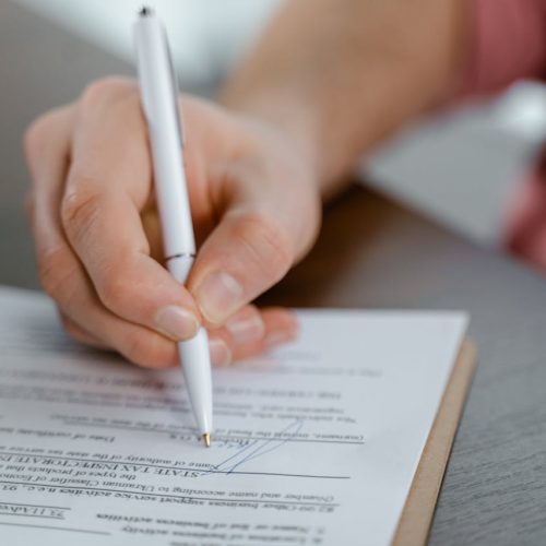 Detailed view of a hand writing a signature on an official document with a ballpoint pen.